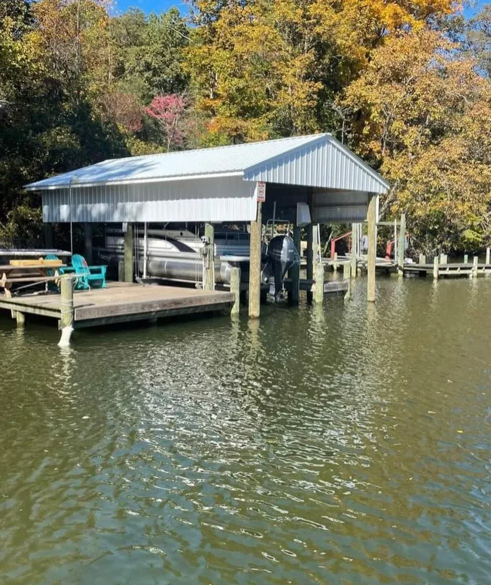A boathouse and pier with a boat on the lift and fall color behind