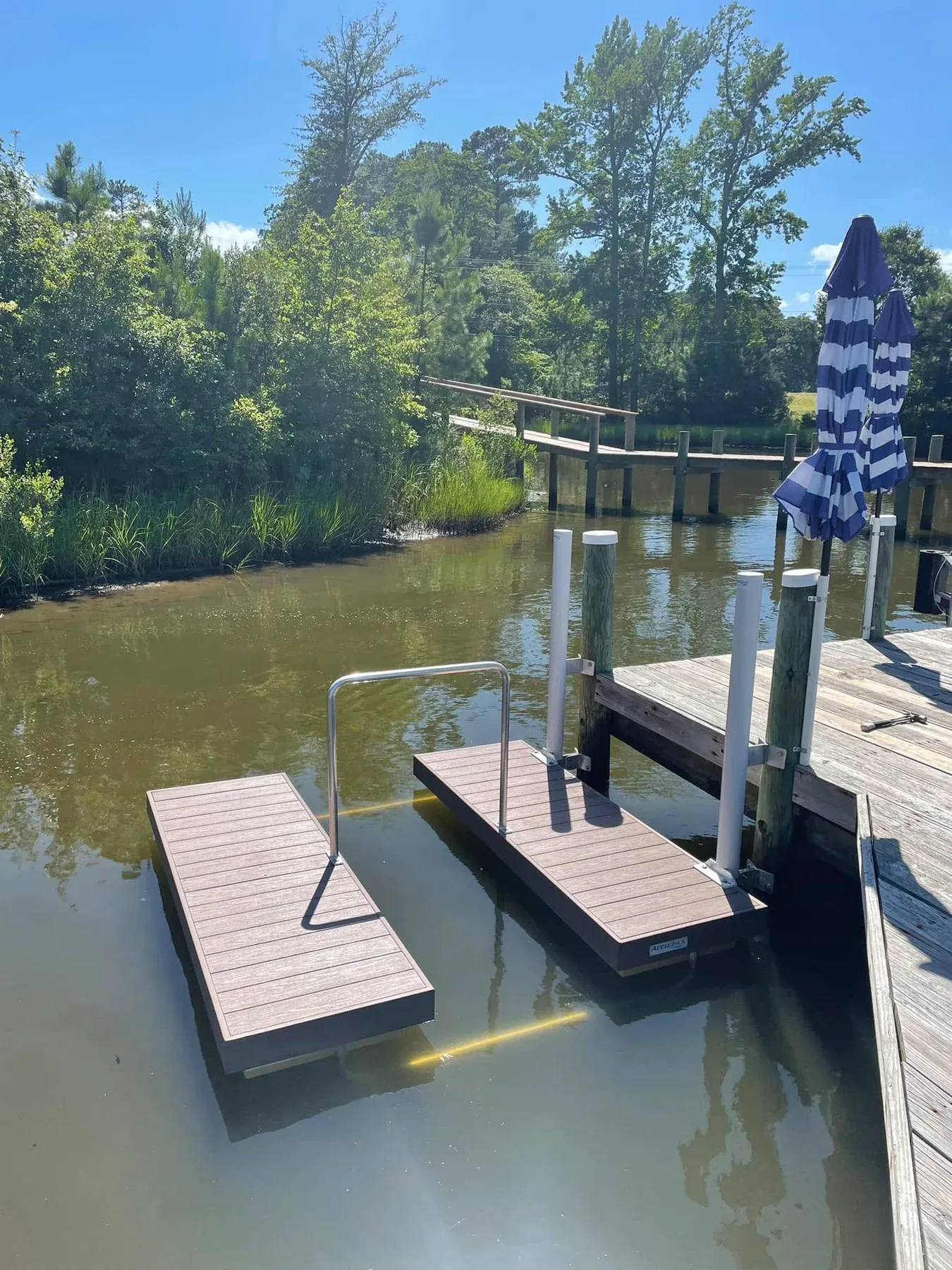 A floating kayak launch with a handrail beside a pier on a creek