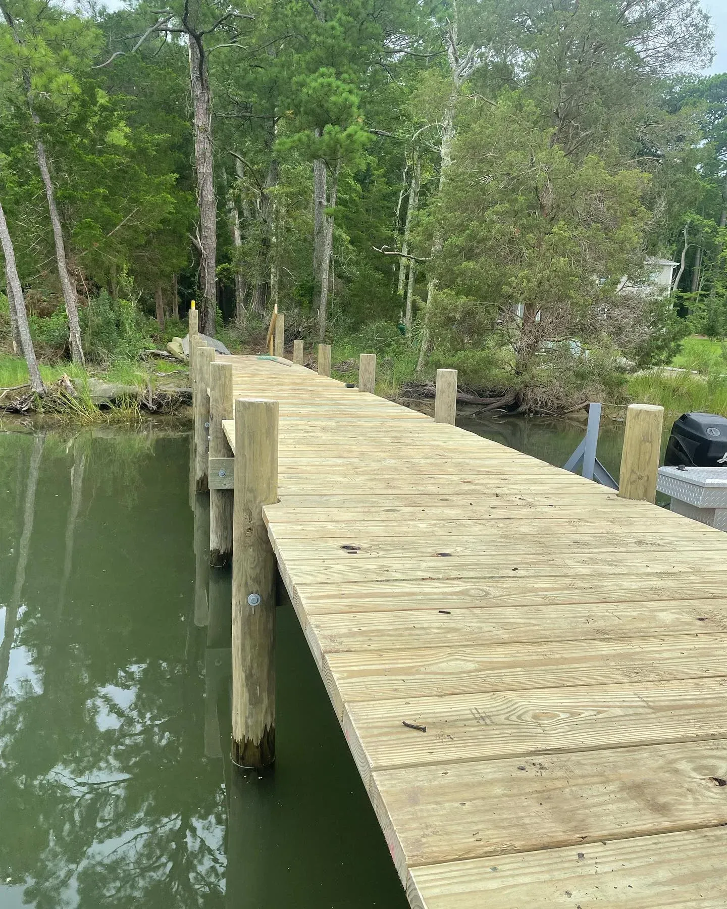 A new wooden pier running from the trees out into a quiet creek