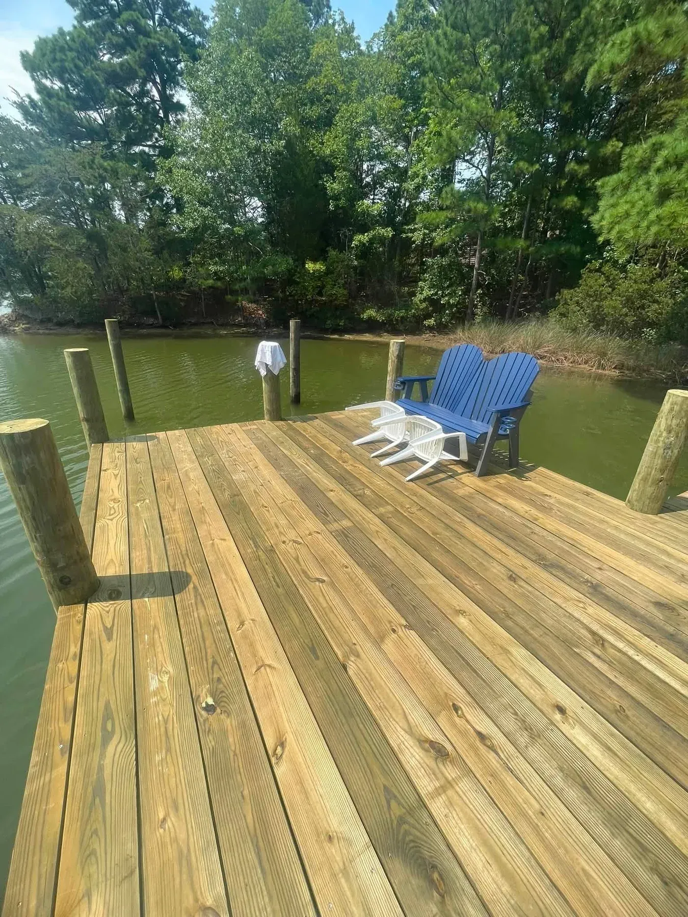 A new pier head platform with blue Adirondack chairs on a wooded creek