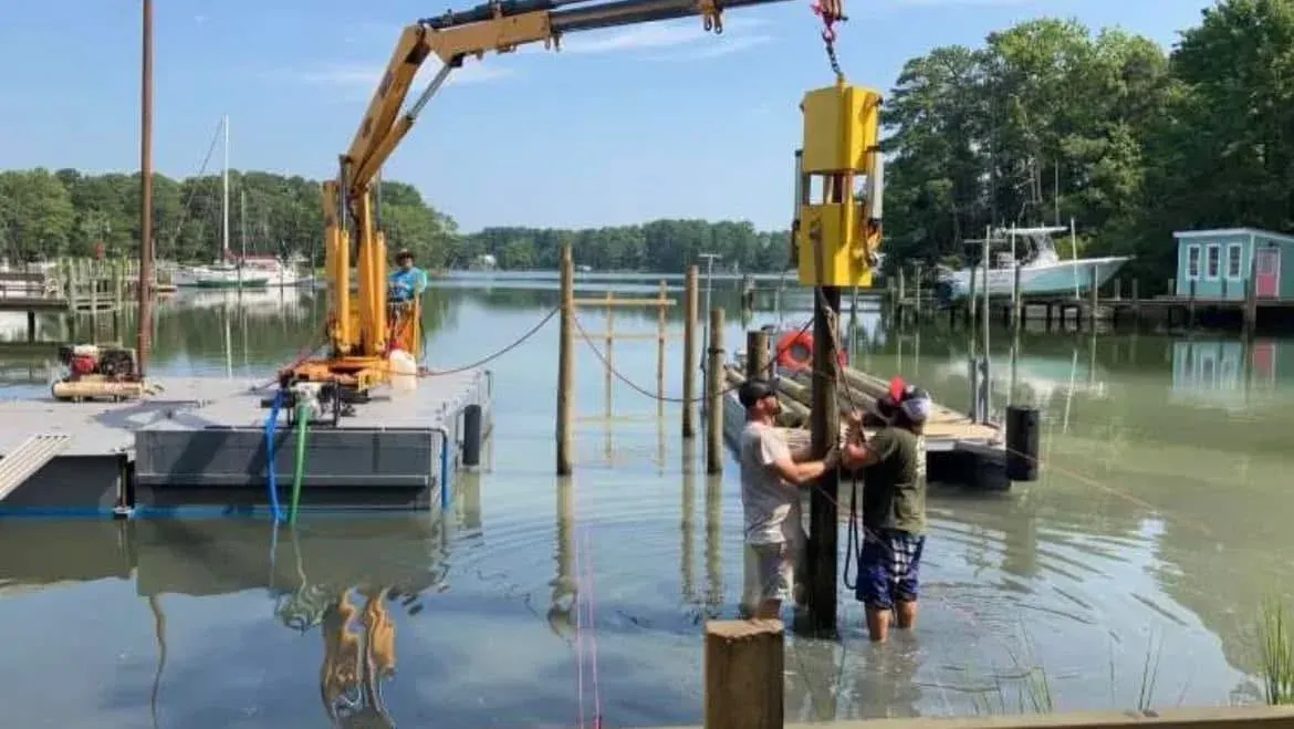 The crew standing in the water guiding a piling into place under the barge crane
